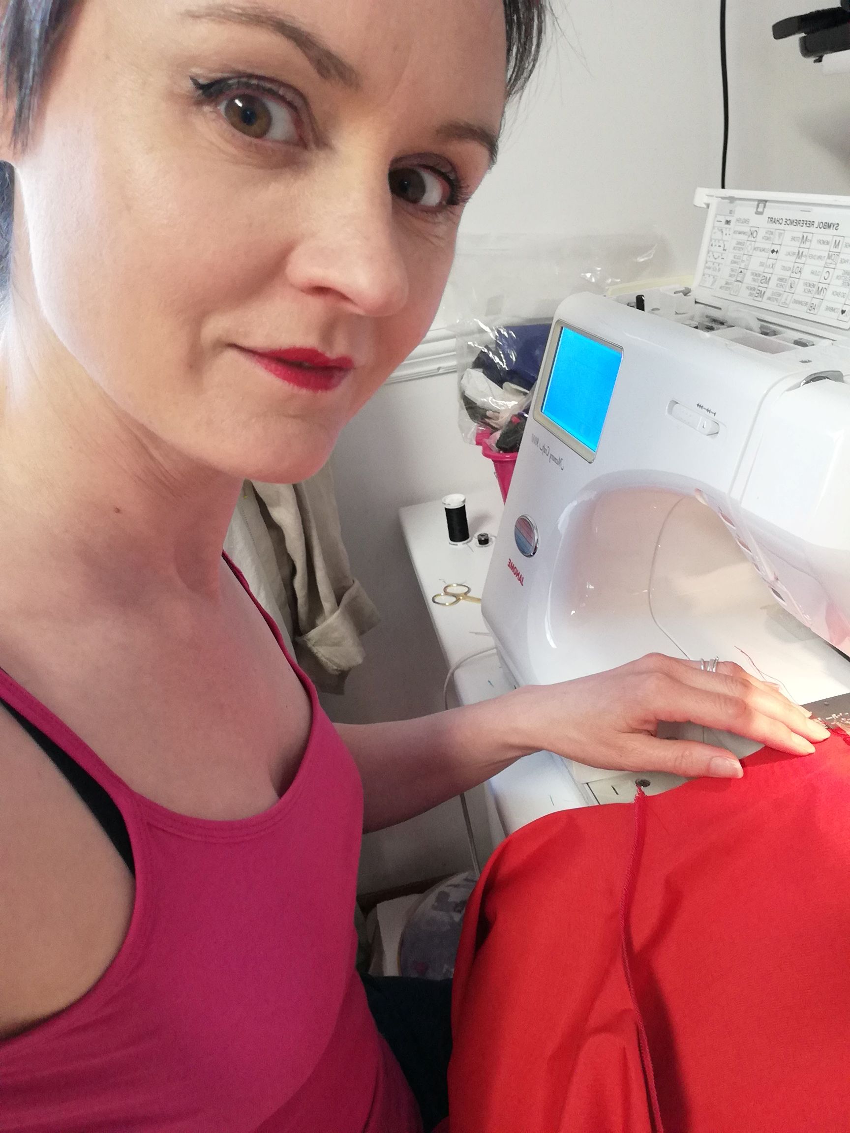 The designer sitting at a sewing machine, looking up at the camera