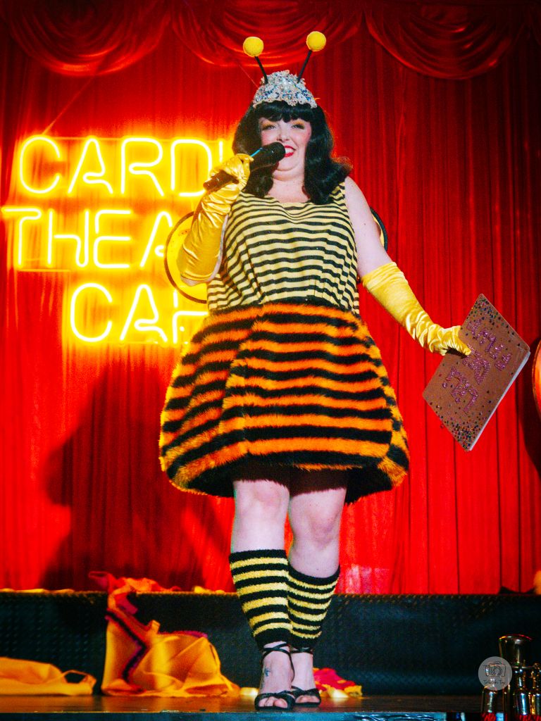 Woman dressed as a bee, holding a mic on stage